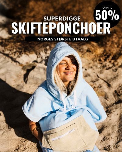 Deilig og varm i en god skifteponcho. Jente smiler på stranden.